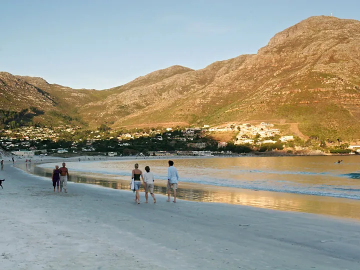 People walking along Hout Bay beach in golden evening light