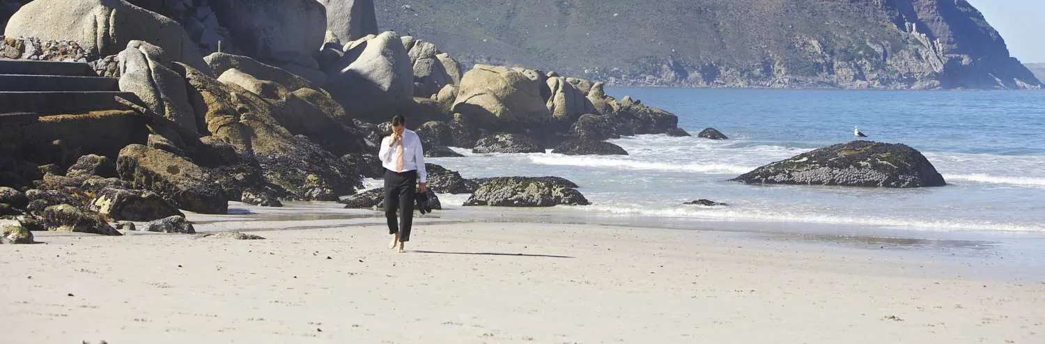 A guest walking barefoot on Hout Bay beach beside the granite boulders